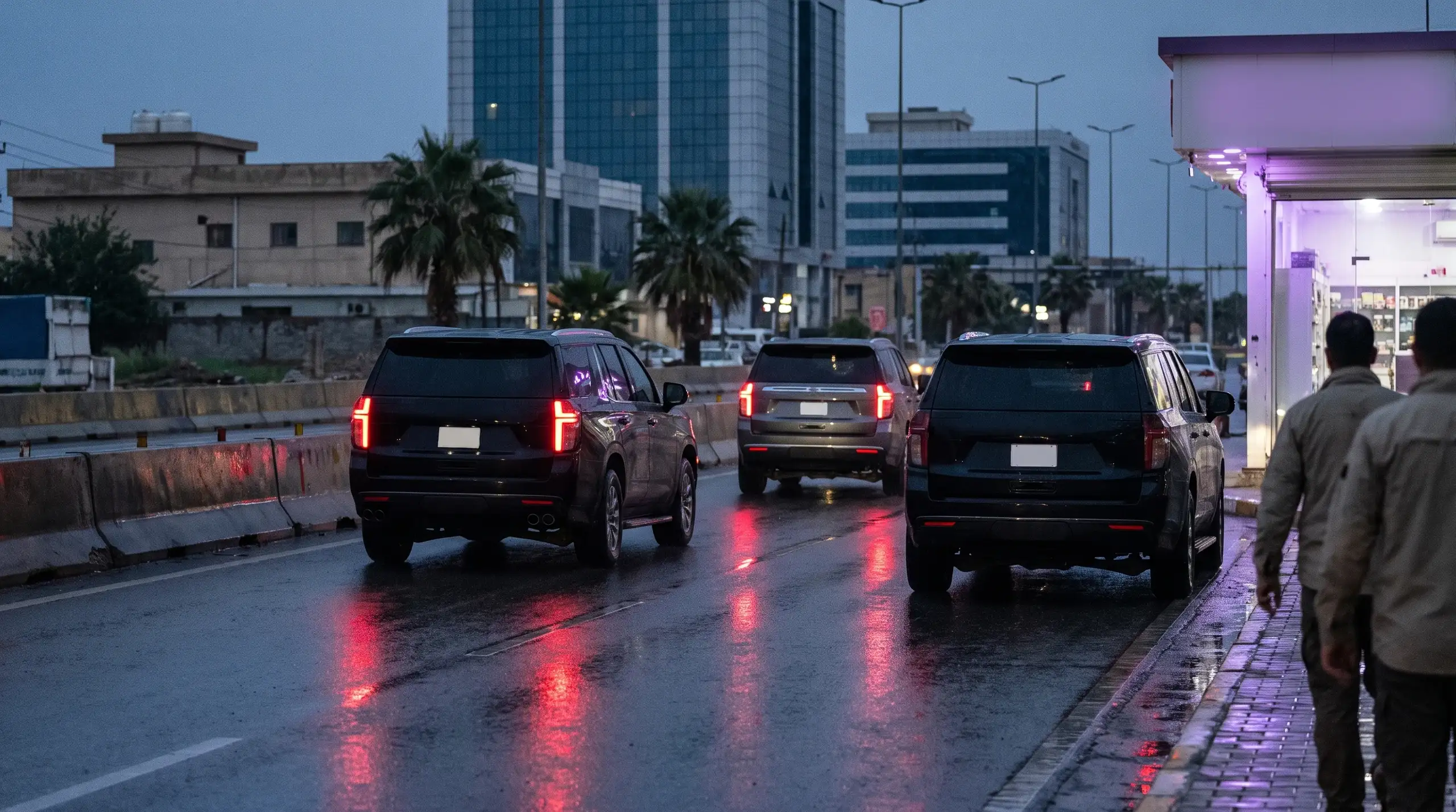 Three dark SUVs on a wet road at dusk
